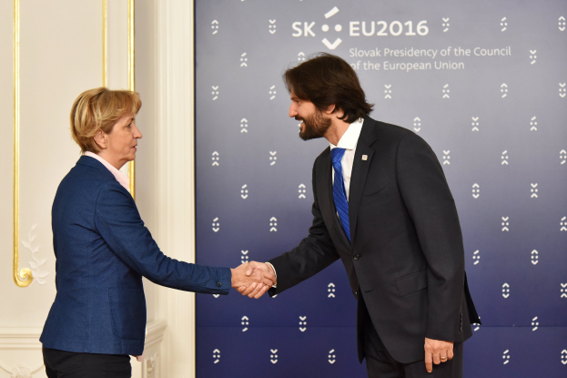 Bundeskanzlerin Angela Merkel und Joachim Gauck schütteln sich warm die Hand vor einer Wand mit einem "EU-Gipfel"-Schild und einer Tür im Hintergrund.