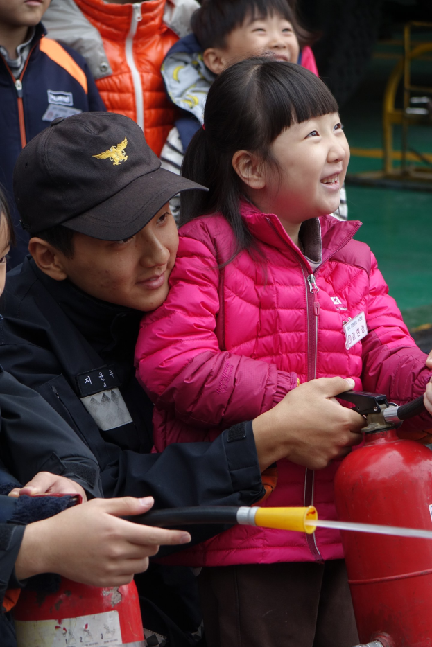 Kinder in einer Schulumgebung versammelt um einen roten Hydranten, einer hält ein Rohr.