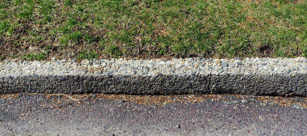 Eine Straße mit einem Kiesrandstein in der Mitte, flankiert von Gras und Steinen.