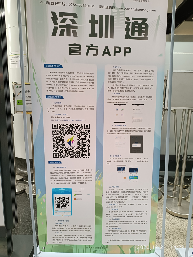 Ein Banner mit einem QR-Code, der den Shenzhen International Airport bewirbt, vor einem Gebäude mit verschiedenen Ständen und Tafeln.