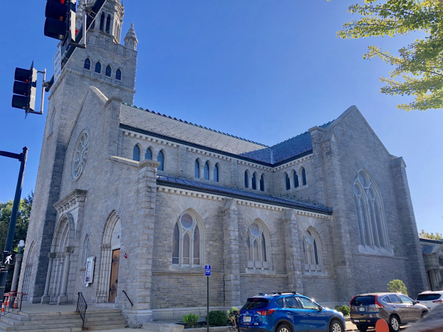 Große steinerne Kirche namens St. Mary's Episcopal Church mit einem Glockenturm, umgeben von Gebäuden, Fahrzeugen, Fußgängern und Bäumen unter einem bewölkten Himmel.