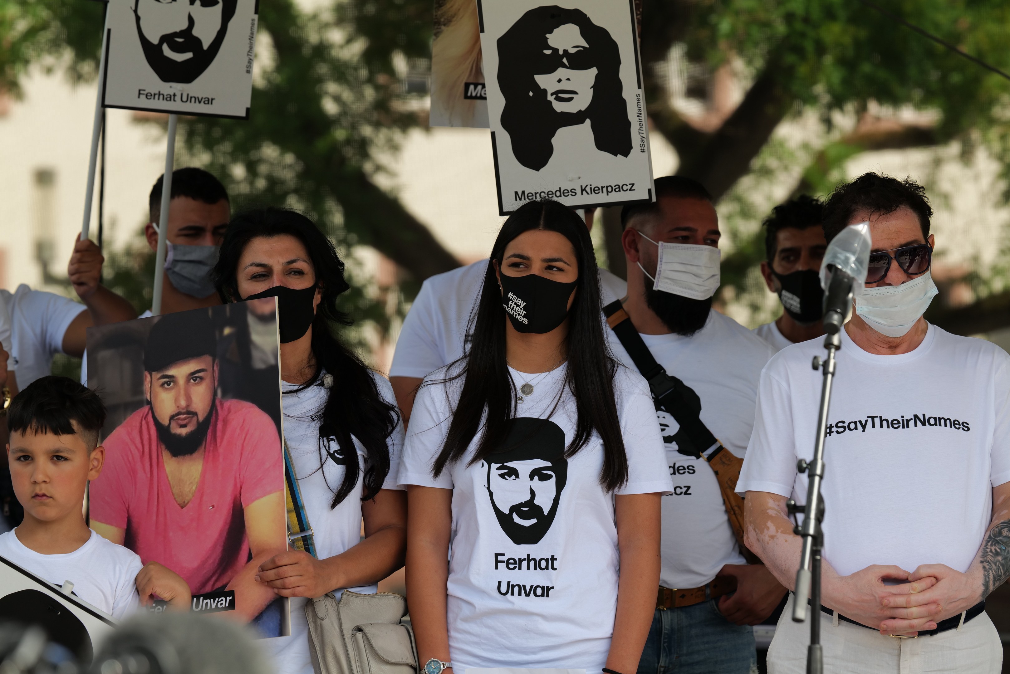 Eine Gruppe von Menschen in Masken und mit Schildern auf einer Demonstration in Mexiko-Stadt, mit einem Mikrofon und einer Kamera im Vordergrund und Bäumen und Gebäuden im Hintergrund.