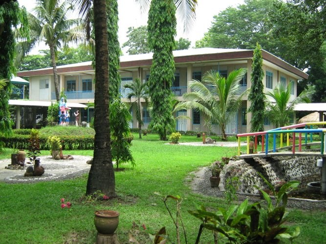 Resorthotel mit grünem Rasen, Bäumen, Pflanzen und einer Brücke, die darauf führt, mit ein paar Menschen in der Nähe unter einem sichtbaren Himmel.