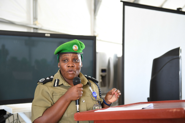 Eine Frau in einer Polizeiuniform steht an einem Podium mit einem Mikrofon, hält ein Papier in der Hand, mit Monitoren und anderen Gegenständen im Hintergrund.