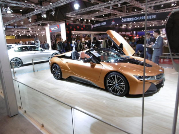 Ein schicker schwarzer BMW i8 Roadster mit Chromakzenten auf der Frankfurt Motor Show umgeben von formell gekleideten G├Ąsten in einer Atmosph├Ąre der Aufregung.
