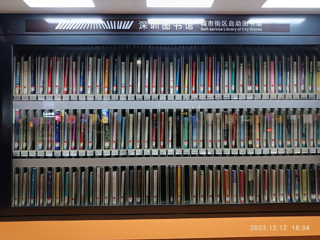 Eine gut beleuchtete Bibliothek mit hohen Bücherregalen voller Bücher, mit einer Texttafel und einem Wasserzeichen unten, ähnlich einer Selbstbedienungsbibliothek von Stadtblöcken.