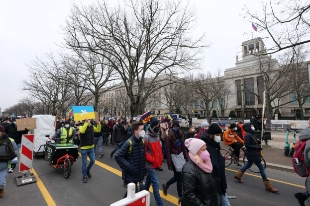 Eine große Gruppe von Menschen marschiert auf einer Straße in Washington, D.C. am 21. Januar 2020, mit Schildern und Bannern, einige fahren Fahrráder, mit Bäumen und einem klaren blauen Himmel im Hintergrund.