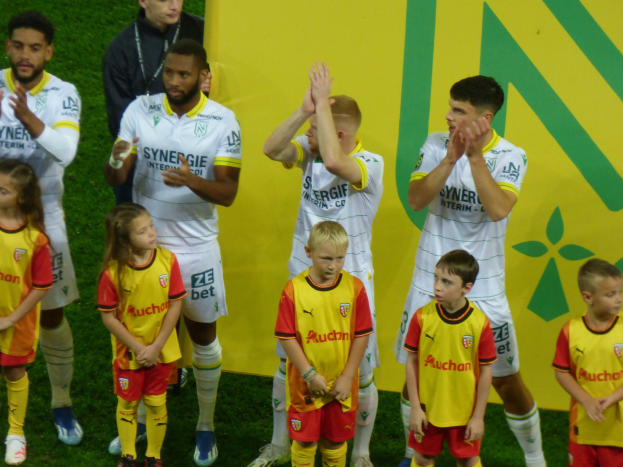 Eine Gruppe von Füßballspielern in Uniformen, die auf einem Feld mit einem "Ligue 1"-Schild im Hintergrund klatschen und einen Sieg feiern.