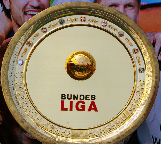 Goldener Schild mit "Bundesliga"-Text in der Hand eines Mannes, mit einem Banner im Hintergrund mit drei Personen.