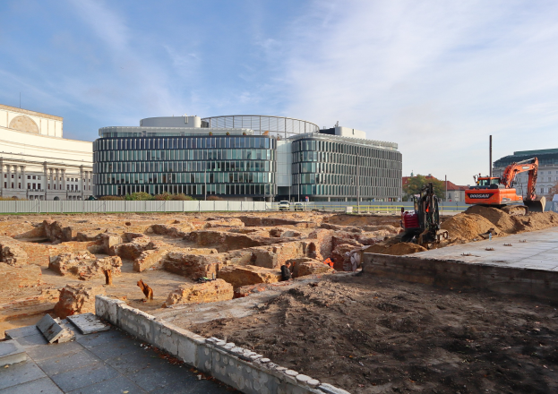Baustelle in Berlin, Deutschland, mit einem großen Gebäude im Bau, umgeben von Fahrzeugen, Arbeitern und der Berliner Mauer.