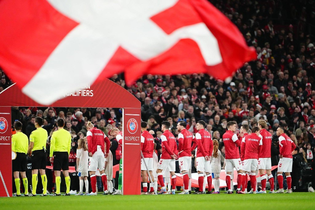 Gruppe von Menschen auf einem Fußballfeld mit einer roten und weißen Flagge im Vordergrund, einem Bogen mit der Aufschrift "Bayern Munich vs. Bayern Munich Wett-Tipps & Vorschau" im Hintergrund und einer großen Menge im Stadion.