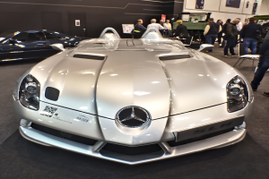 Ein Mercedes-Benz SLR McLaren Roadster wird auf dem Genfer Auto-Salon präsentiert, umgeben von mehreren Bewunderern, die Wand des Ausstellungsraums ist mit Plakaten und Lichtern geschmückt.