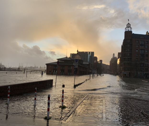 Überschwemmte Straße in Hamburg, Deutschland mit Wasser, das die Straße, Pfosten, Schilder, Gebäude und eine Brücke bedeckt.