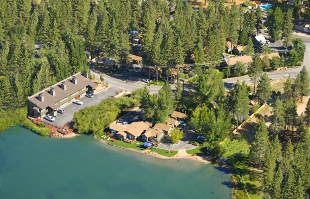 Luftbild eines Resorts am Seeufer mit umliegenden Bäumen, Häusern, Fahrzeugen, Straßen, Masten und Gras, mit dem See unten sichtbar.