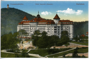 Eine alte Ansichtskarte des Hotel Imperial in Karlsbad, Deutschland, zeigt ein großes Gebäude mit Fenstern, umgeben von Bäumen, Pflanzen, Gras, einem Pfad, einer Gruppe von Bäumen, Hügeln und einem bewölkten Himmel, mit Text oben.