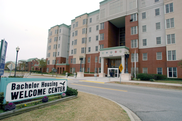 Ein Willkommenszentrum für Bachelor-Wohnungen mit Gebäuden, Straßenlaternen, Straßenlaternen, Schildern, Fahrzeugen, Grünflächen und einem klaren Himmel.