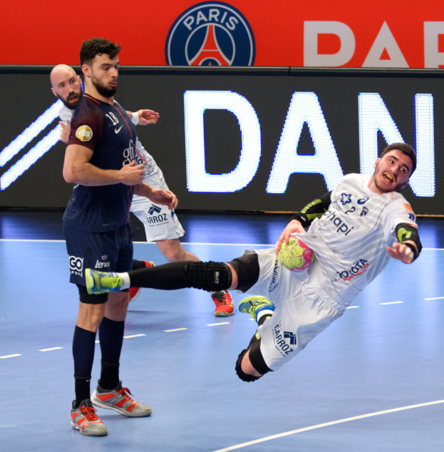 Eine Gruppe von Männern, die Handball auf einem Platz spielen, einer hält den Ball, im Hintergrund ein Paris Saint-Germain-Futsal-Team-Schild.