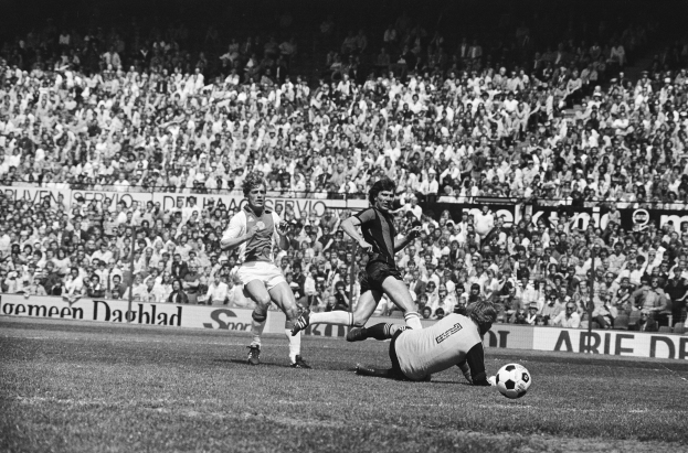 Schwarzes Foto von Männern, die auf einem Feld Füßball spielen, mit Zuschauern im Hintergrund und einer Fahne mit der Aufschrift "Bundesliga 1978-79 Ajax 1-1 Hannover 96".