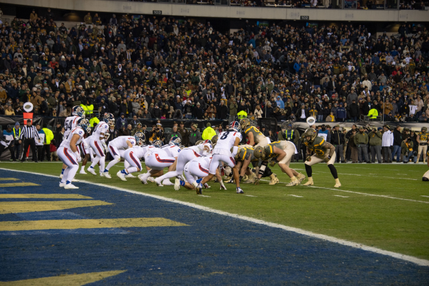 Ein Fußballspiel im Gange mit Spielern auf dem Boden in Sportbekleidung und Helmen, aus der Sicht eines Stadionplatzes.