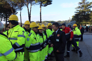 Eine Gruppe von Einsatzkräften in gelben Westen und Helmen, die auf einer Straße mit Bäumen und einem klaren blauen Himmel stehen.