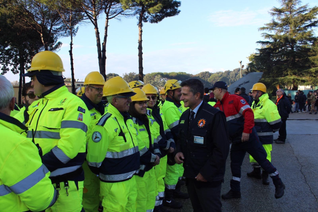 Eine Gruppe von Einsatzkräften in gelben Westen und Helmen, die auf einer Straße mit Bäumen und einem klaren blauen Himmel stehen.