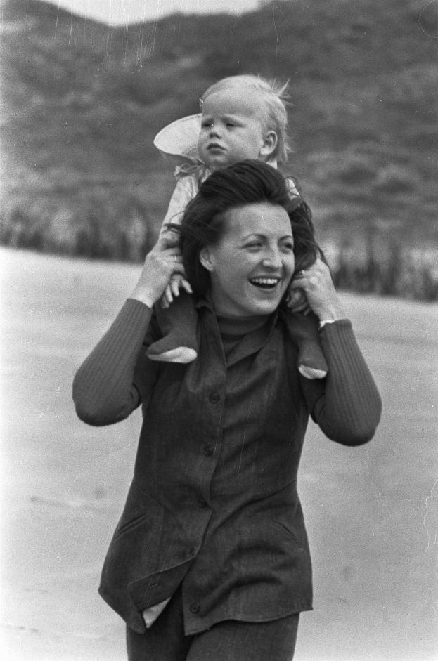 Eine Frau lächelt warm, während sie ein Baby hält, mit einem sanft unscharfen Hintergrund, der einen nostalgischen Effekt erzeugt.