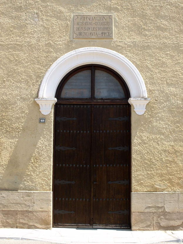 Alte hölzerne Tür mit einem Namensschild darüber, die wahrscheinlich den Eingang zu einem Krankenhaus markiert, in einem steinernen Gebäude mit einer Straße unten.