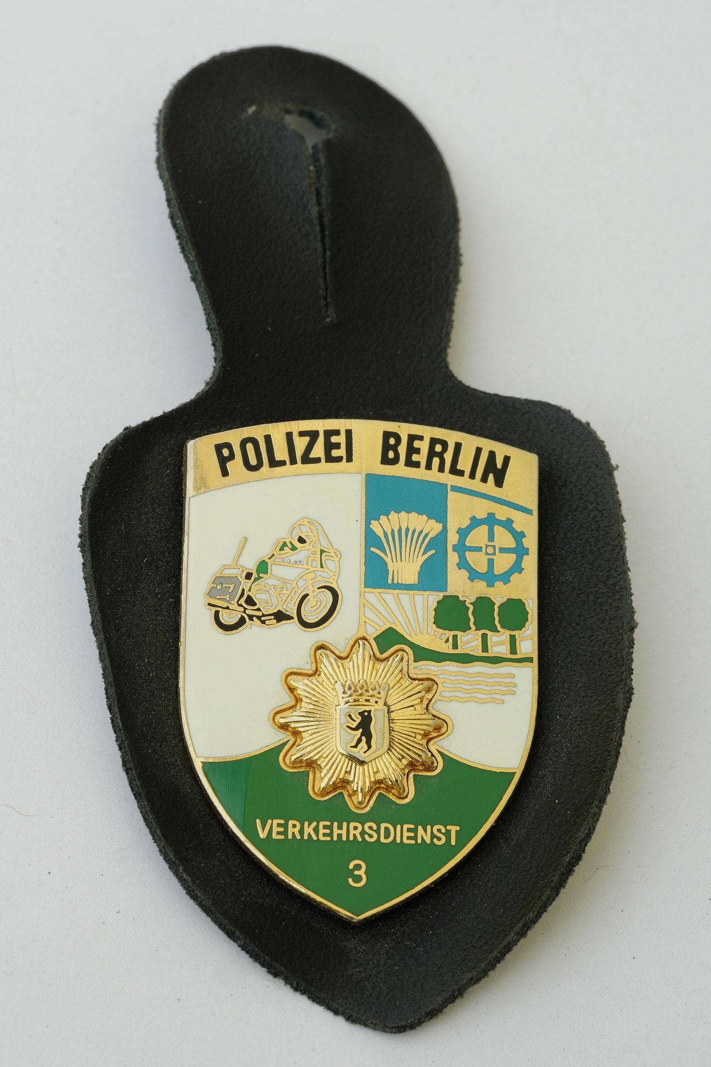 Ein schildförmiges Polizeibädgetä mit "Polizei Berlin" in schwarzer fetter Schrift, das ein weißes Stern auf einem blauen Hintergrund mit einem weißen Rand zeigt, liegt auf einer Oberfläche.