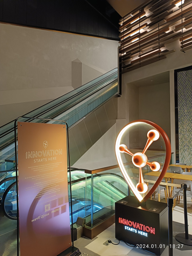 Großes Schild mit der Aufschrift "Innovation Starts Here" in einem Gebäude mit einem Aufzug im Hintergrund, Tische und Stühle auf der rechten Seite und ein Expo-Schild auf der linken Seite.