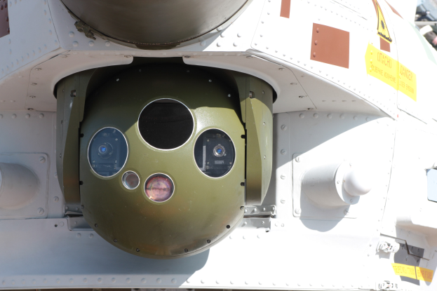 Ein militärisches Fahrzeug mit einer runden, grünen und weißen Rakete, die an seiner Seite befestigt und von einem Metallrahmen umgeben ist.