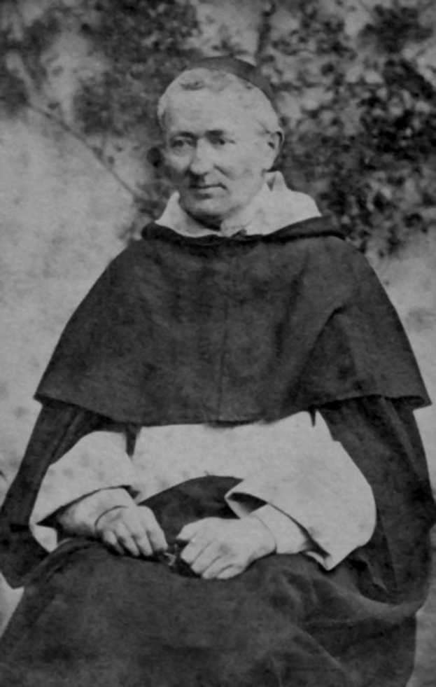 Ein Schwarz-Weiß-Foto eines alten Mannes in Priesterkleidung, der im Freien mit gefalteten Händen betet und von warmem Licht erhellt wird.