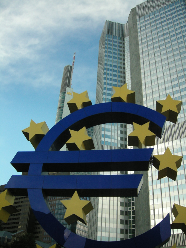 Eurozeichen vor dem Gebäude der Europäischen Zentralbank in Frankfurt, Deutschland, mit Bäumen und einem bewölkten Himmel.