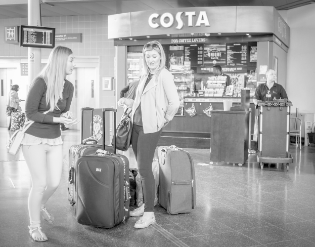 Zwei Frauen mit Gepäck vor einem Café in einer Umgebung, die wie ein Flughafen aussieht.