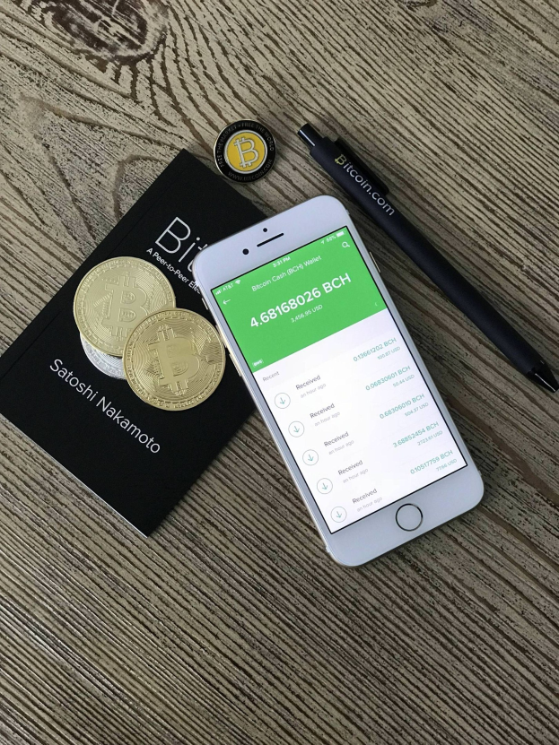 Ein Holztisch mit einem Handy, das die Bitcoin Cash Wallet App anzeigt, einem Buch und einem Stift.