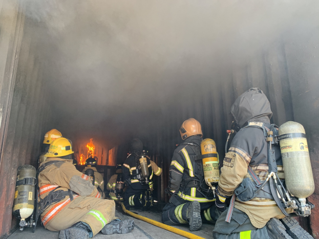 Feuerwehrleute in Helmen und Sauerstoffflaschen sitzen im Heck eines raucherfüllten Lkws in der Nähe eines große Feuers während einer Übungsstunde an der University of California, Berkeley.
