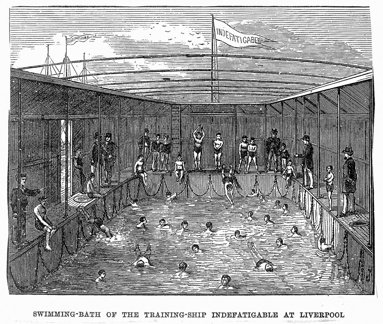 Ein Schwimmbad mit einem "Nur für Erwachsene - Nichtschwimmerbereich"-Schild im Vordergrund, umgeben von Bäumen und Gebäuden unter einem klaren blauen Himmel, mit einem Rettungsring in der Mitte des Pools.