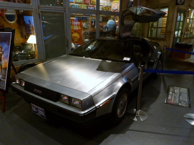 Ein DeLorean DMC-12 aus der Zurück in die Zukunft-Franchise wird in einem Museum ausgestellt, umgeben von Informationsanzeigen, Bändern und verschiedenen anderen Gegenständen.