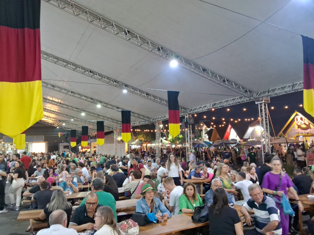 Große Gruppe von Menschen an langen Tischen unter einem Outdoor-Zelt auf dem Oktoberfest in München, Deutschland, mit festlicher Dekoration im Hintergrund.