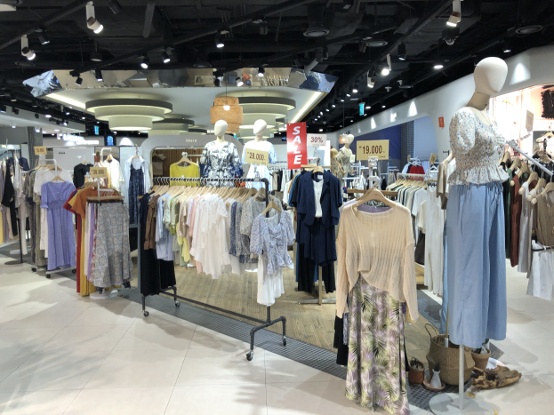 Ein Bekleidungsgeschäft mit Schaufensterpuppen in Kleidern an Kleiderbügeln, beleuchtet von Deckenlampen und verschiedenen Schildern und Bodenartikeln, die auf einen Modegeschäft hinweisen.