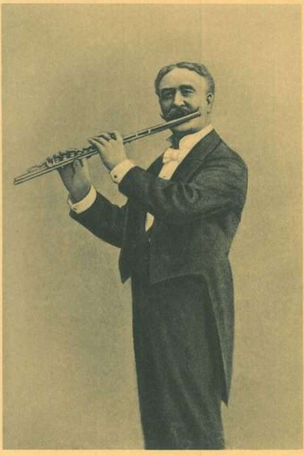 Ein Schwarz-Weiß-Foto eines älteren Mannes in einem Smoking, der auf der Bühne eine Flöte spielt und die Augen geschlossen hat.