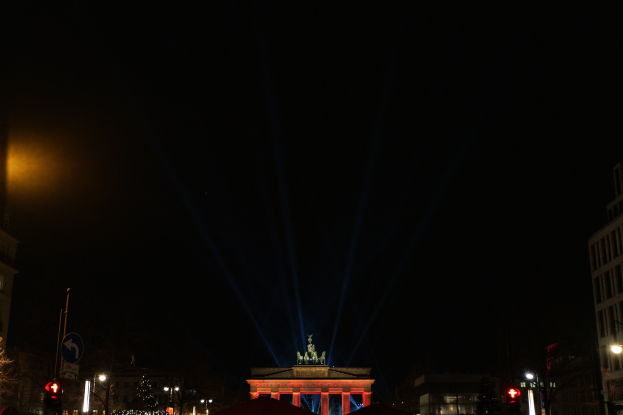 Brandenburger Tor bei Nacht, beleuchtet von Straßenlaternen, mit umliegenden Gebäuden, Bäumen, Polen, Verkehrszeichen, Schildern und Zelten gegen einen dunklen Himmel.