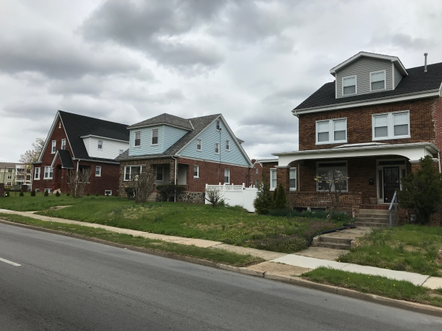 Eine Reihe von H├Ąusern in Renovierung, mit Werkzeugen und Materialien ├╝berall verstreut, mit Fenstern, T├╝ren, Stufen, Gel├Ąndern, Pflanzen, Gras, B├Ąumen und einem bew├Âlktem Himmel im Hintergrund.